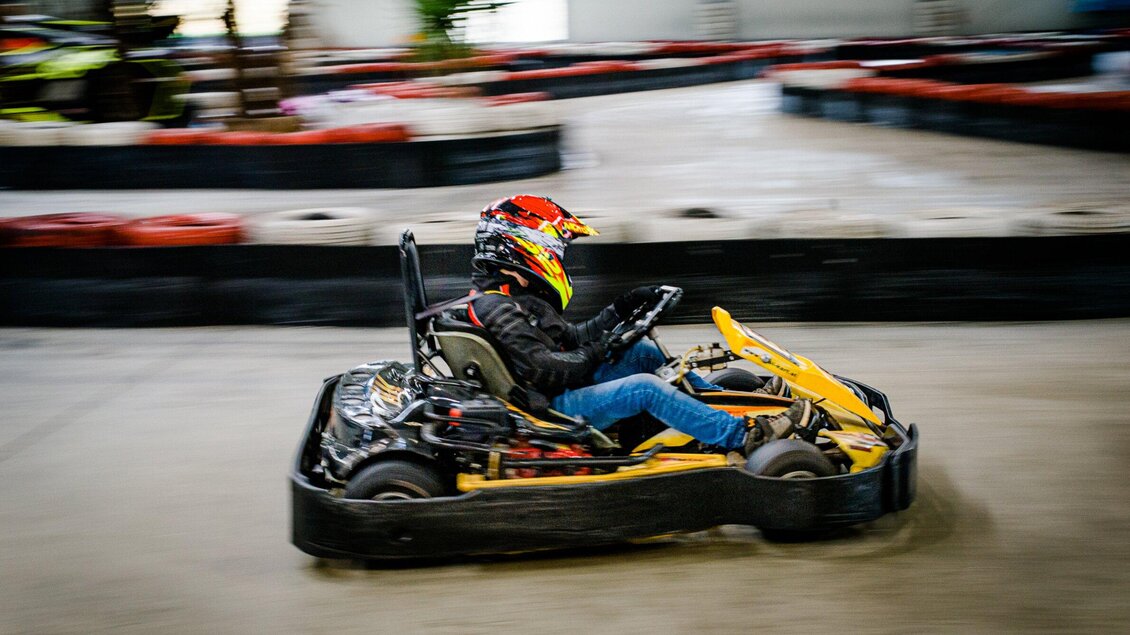 Ein Kartfahrer fährt schnell auf einer Kartbahn. Die Umgebung ist indoor mit verschiedenen Rennstrecken. | © TV Region Graz - Mias Photoart