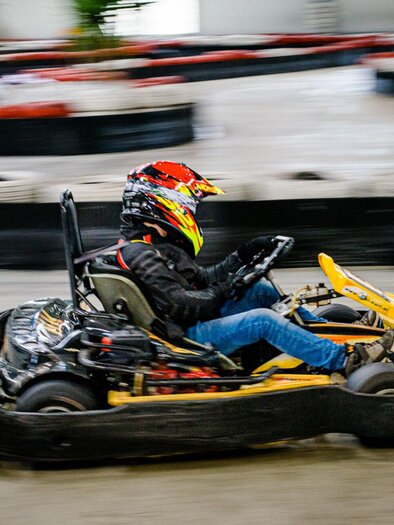 A go-kart driver is speeding on a go-kart track. The environment is indoors with various racetracks. | © TV Region Graz - Mias Photoart