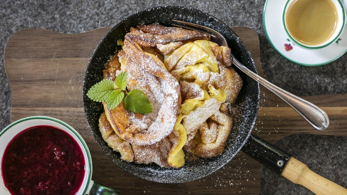 Ein leckeres Gericht in einer Pfanne, bestehend aus gebratenem Brot, bestäubt mit Puderzucker und garniert mit frischer Minze. Dazu gibt es eine Tasse Kaffee und eine Schüssel mit roter Fruchtsoße. | © Seewiese Altaussee