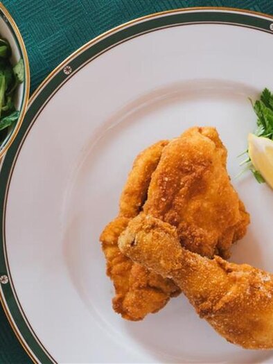 A plate with crispy, fried chicken and a piece of lemon. Next to it is a bowl with a fresh salad. | © AdobeStock