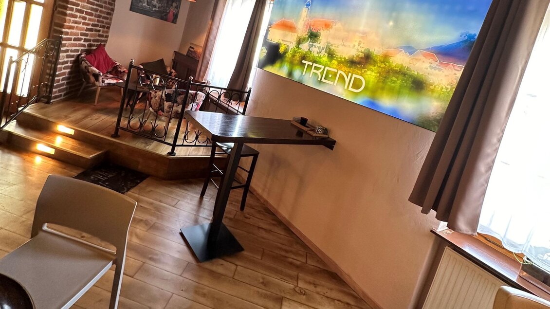 Ein gemütlicher Innenraum mit Holzboden und einem modernen Kunstwerk an der Wand. Es gibt einige Sitzgelegenheiten und viel Tageslicht. | © TREND