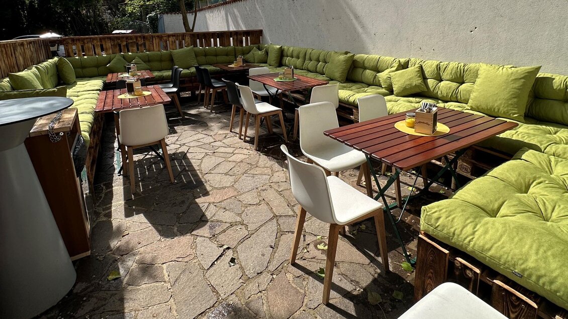 Ein gemütlicher Außenbereich mit bequemen, grünen Sitzpolstern und kleinen Tischen. Es ist ein einladender Ort zum Entspannen und Genießen. | © TREND