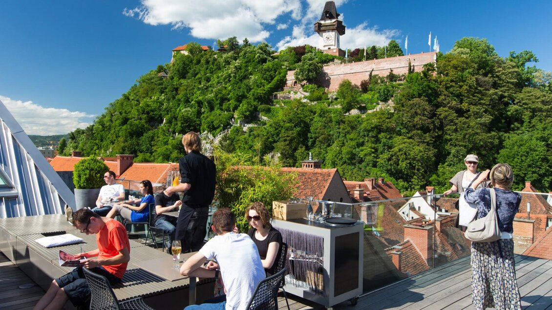 Gäste genießen Drinks und Aussicht auf Schlossberg und Uhrturm von der Dachterrasse des Tagescafé Freiblick | © Graz Tourismus - Harry Schiffer