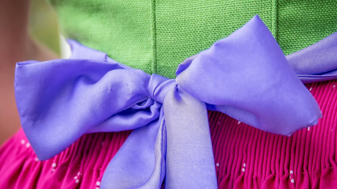 Ein bunter Trachtenrock mit einem lila Schleifenband. Der Rock hat eine pinke Farbe und eine strukturierte grüne Oberseite. | © www.narzissenfest.at_Christine Struz