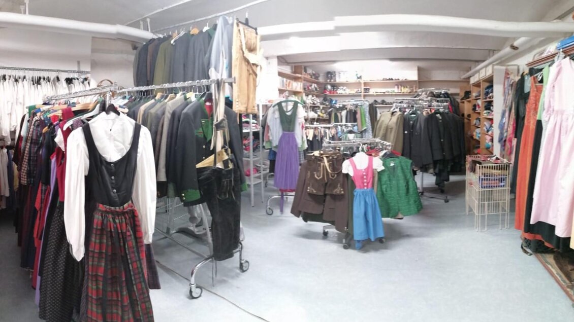 Ein Bekleidungsgeschäft mit verschiedenen Trachten und Kleidungsstücken hängt an Kleiderständern. Die Umgebung ist hell und lädt zum Stöbern ein. | © Erika Baumann