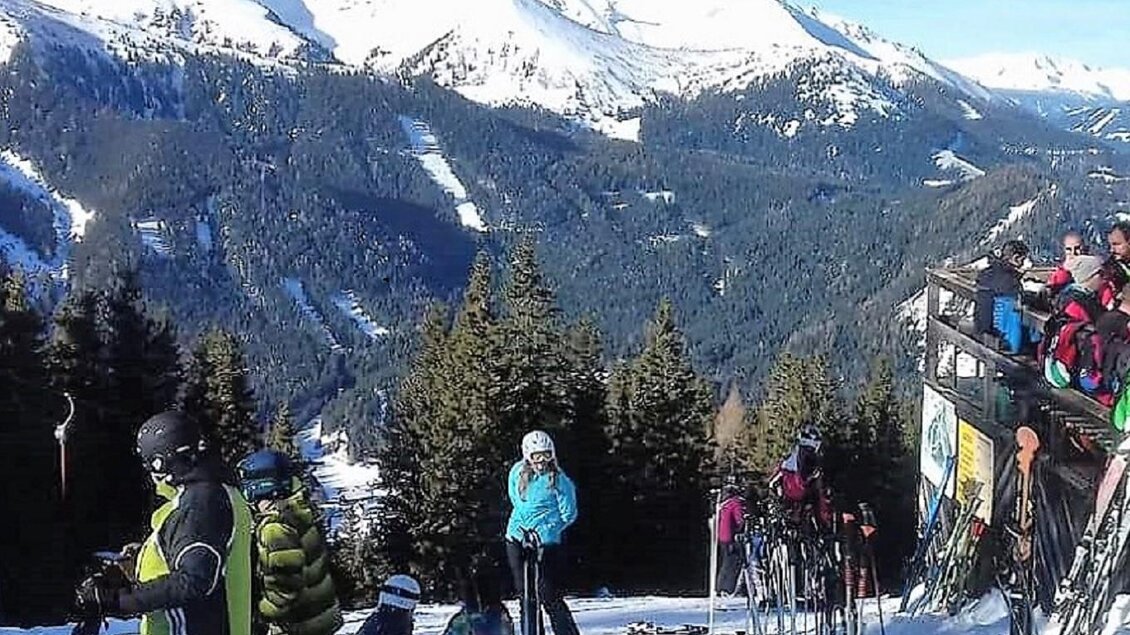 Eine verschneite Berglandschaft mit Skifahrern und einer klaren blauen Himmel. Im Vordergrund stehen mehrere Skier und Menschen, die auf der Skipiste warten. | © Erlebnisregion Murtal