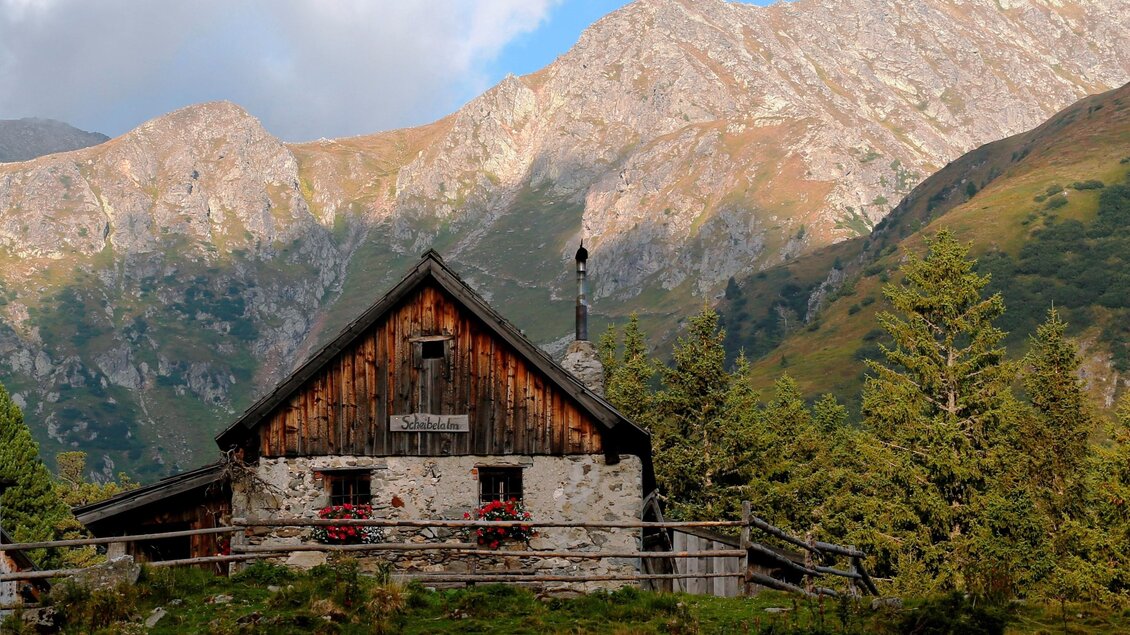 Ein gemütliches Holzhaus liegt in einer grünen Landschaft mit Bergen im Hintergrund. Der Himmel ist klar mit einigen Wolken. | © Erlebnisregion Murtal