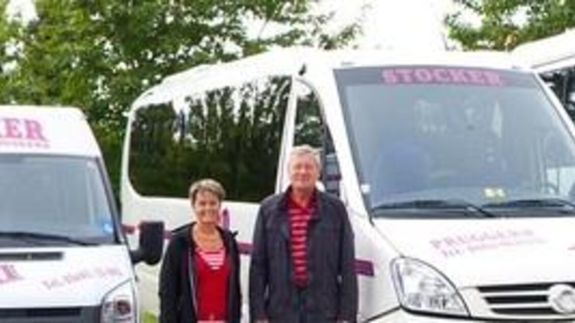 Eine Flotte von Fahrzeugen mit dem Namen "Stocker" steht bereit. Zwei Personen stehen neben den Fahrzeugen in einer grünen Umgebung. | © Taxi Stocker 