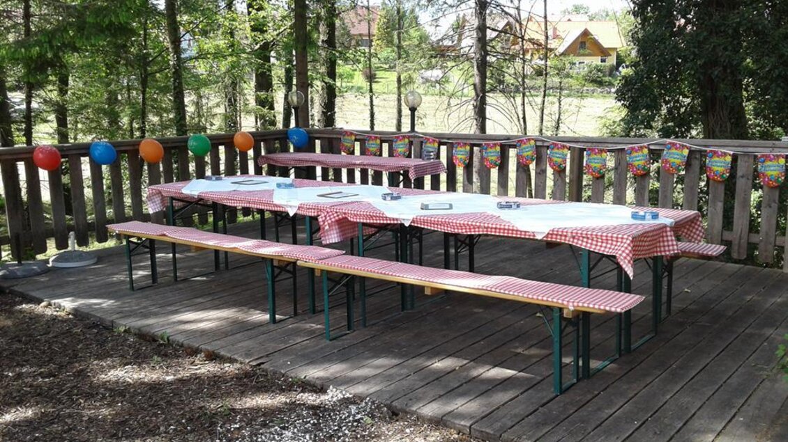 Ein hübscher Außenbereich mit Holztisch und Bänken. Die Tische sind mit rot-weißen Tischdecken dekoriert und der Bereich ist festlich geschmückt. | © Muhri & Platz OG;