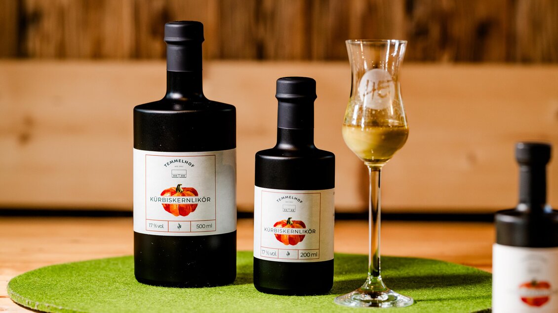 Zwei Flaschen mit dunklem Etikett und einem Glas mit einer Flüssigkeit stehen auf einem runden grünen Teppich. Im Hintergrund sind Holzwände sichtbar. | © Region Graz - Mias Photoart