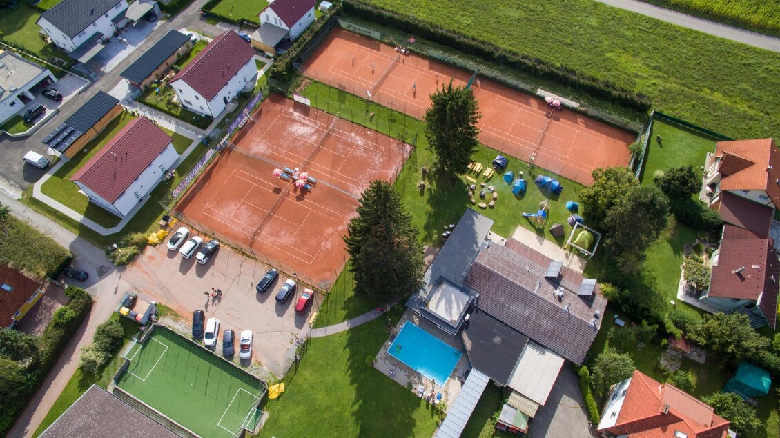 Eine Luftaufnahme von einem Sportgelände mit zwei Tennisplätzen und einem Swimmingpool. Umgeben von Wohnhäusern und einem Parkplatz. | © Kerim Sijercic