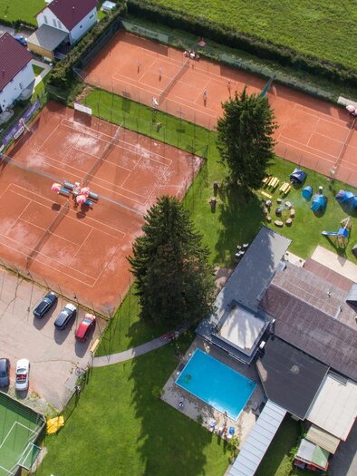 An aerial view of a sports facility with two tennis courts and a swimming pool. Surrounded by residential buildings and a parking lot. | © Kerim Sijercic