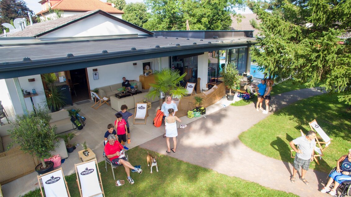Ein einladendes Café mit einer gemütlichen Terrasse und Sitzgelegenheiten im Freien. Menschen und Hunde genießen die Zeit im Grünen. | © Kerim Sijercic