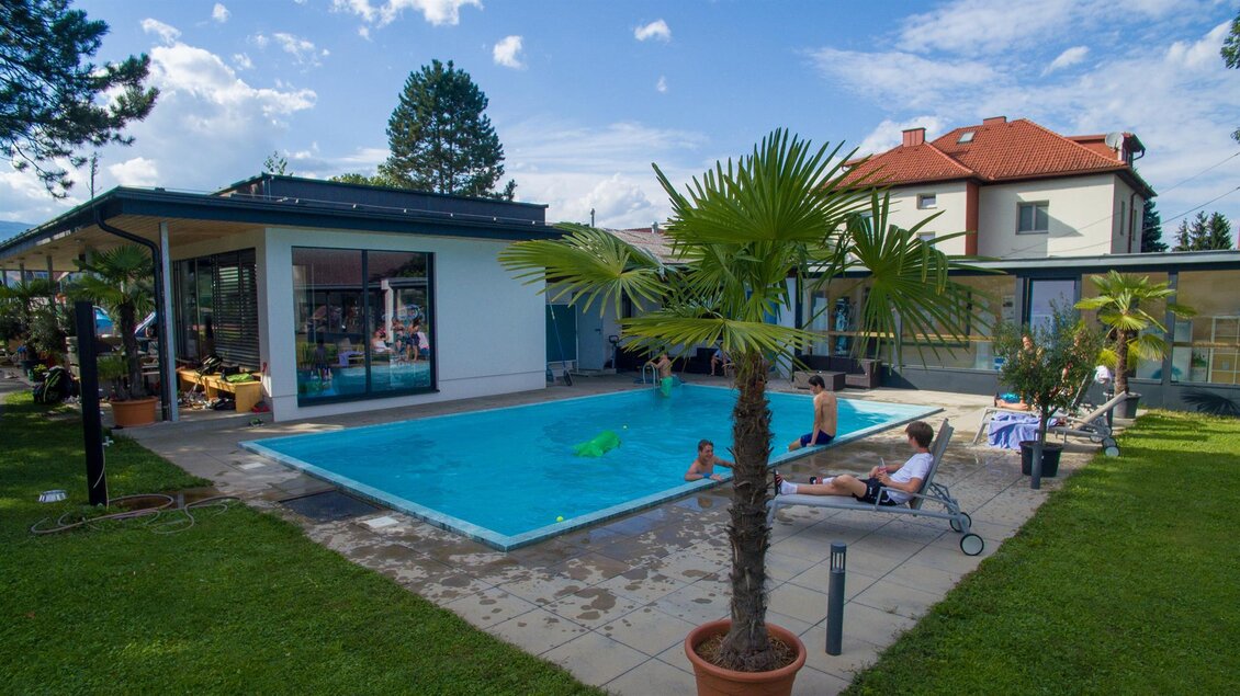 Ein schöner Außenbereich mit einem Pool und Palmen. Menschen entspannen sich auf Liegen und genießen die Atmosphäre. | © Kerim Sijercic