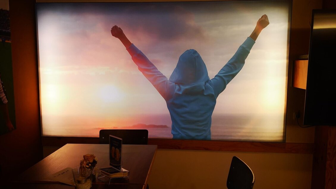 Ein Mensch mit erhobenen Armen steht vor einem Sonnenuntergang. Er trägt einen blauen Kapuzenpullover und wirkt glücklich und triumphierend. | © Kerim Sijercic