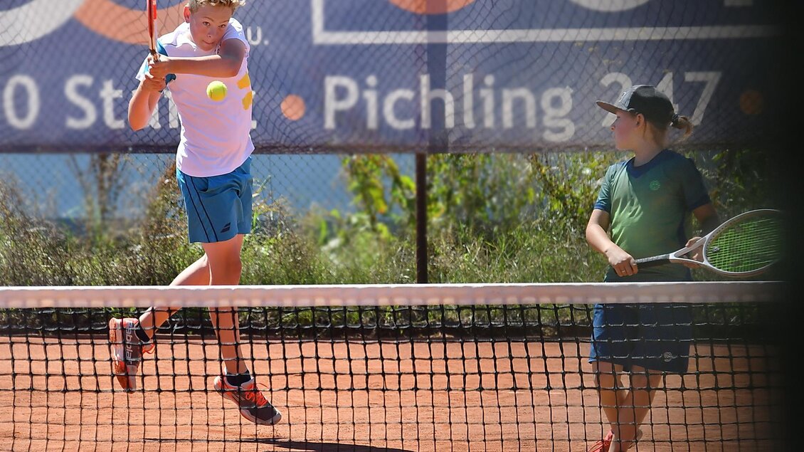 Ein junger Tennisspieler springt über das Netz und schlägt den Ball. Ein weiterer Junge steht auf der anderen Seite des Netzes und wartet, um den Ball zu empfangen. | © Kerim Sijercic