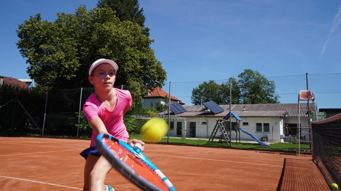 Ein Mädchen spielt Tennis auf einem Außenplatz. Im Hintergrund sind Bäume und ein Gebäude zu sehen. | © Kerim Sijercic