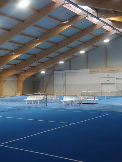 A modern tennis hall with a blue floor and wooden beams. The space is well-lit and ready for games. | © Stadtgemeinde Friedberg