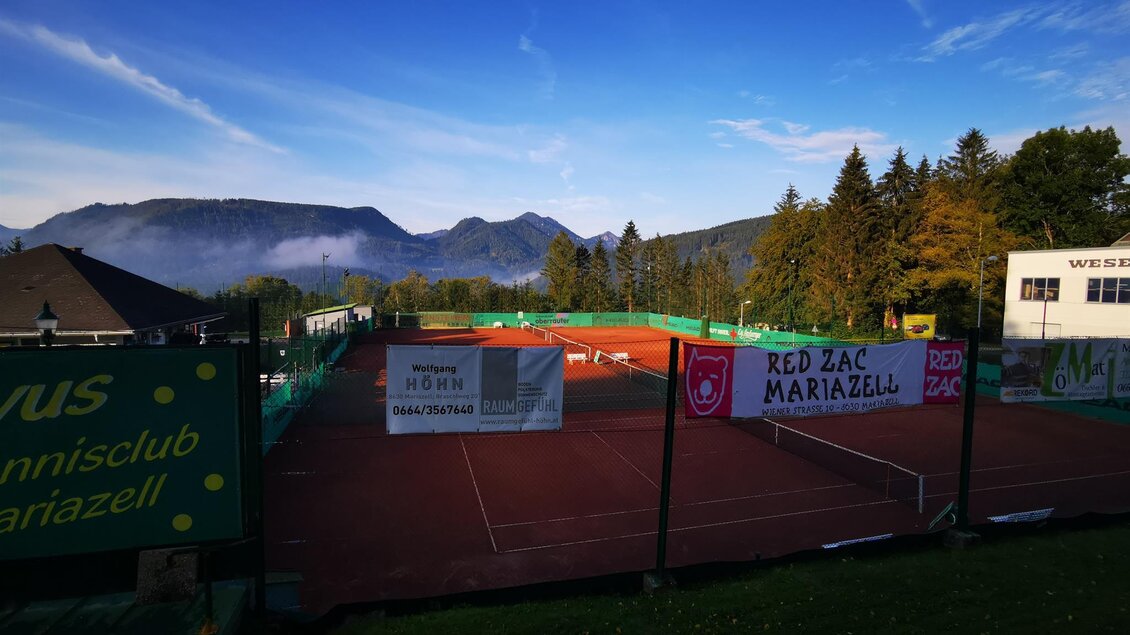 Ein Tennisplatz mit roten Belägen und grünem Netz. Im Hintergrund sind Berge und ein klarer Himmel zu sehen. | © TV Hochsteiermark | Brigitte Digruber