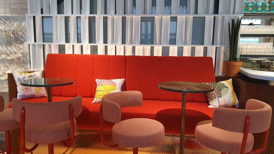 Ein moderner Sitzbereich mit einem roten Sofa und einer hellen Farbpalette. Dazu gehören runde Tische und stilvolle Stühle, die eine gemütliche Atmosphäre schaffen. | © TV Region Graz-Haubenhofer