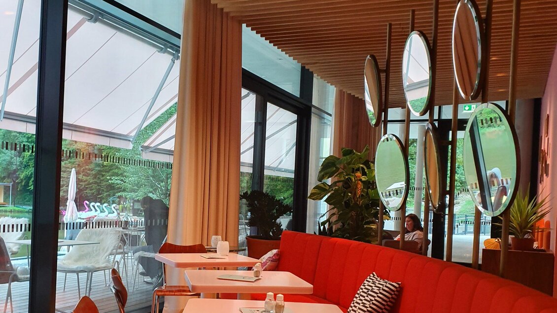 Ein modernes Café mit roten Sofas und großen Fenstern. Im Hintergrund sind Pflanzen und Tische sichtbar, die eine einladende Atmosphäre schaffen. | © TV Region-Haubenhofer