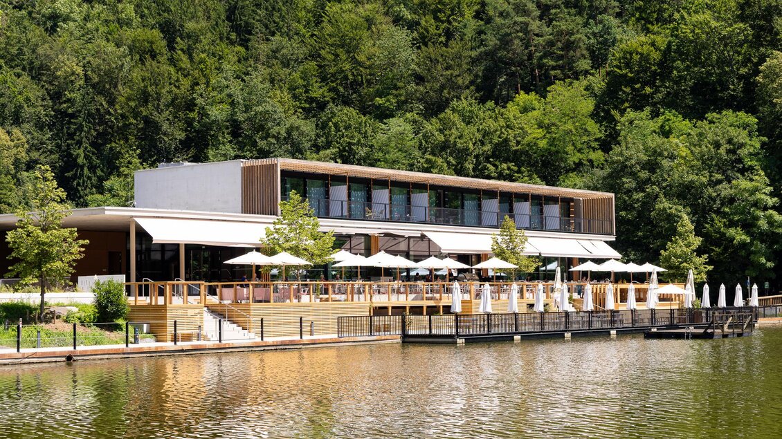 Ein modernes Restaurant am Ufer eines Sees, umgeben von Bäumen. Die Terrasse ist mit Sonnenschirmen ausgestattet und bietet einen schönen Blick auf das Wasser. | © Region Graz, Harry Schiffer