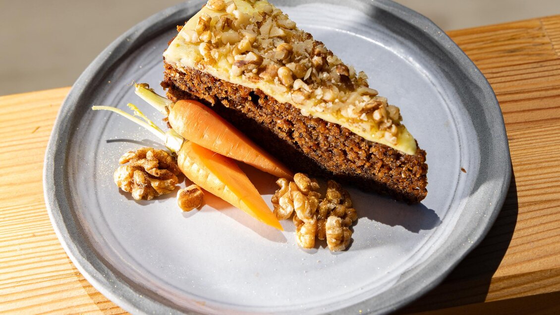 Ein Stück Karottenkuchen mit Walnüssen auf einem grauen Teller. Daneben liegen frische Karotten und einige Walnüsse. | © Region Graz, Harry Schiffer