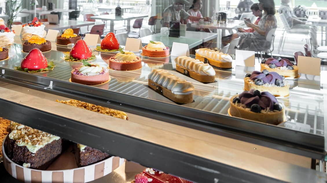 Eine Vitrine voller bunter Torten und Kuchen. Im Hintergrund sitzen Gäste in einem modernen Café. | © Region Graz, Harry Schiffer