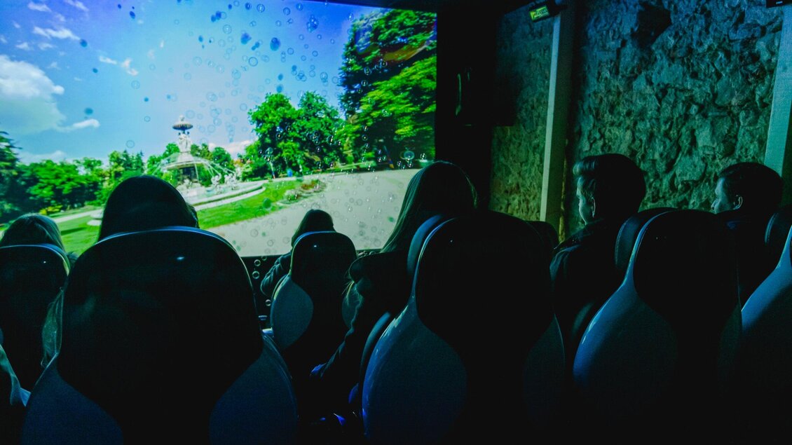 Eine Gruppe von Menschen sitzt in einem Raum mit großen Sitzen und sieht sich eine beeindruckende 3D-Präsentation an. Auf der Leinwand sind Bäume und eine Landschaft zu sehen. | © Region Graz - Mias Photoart