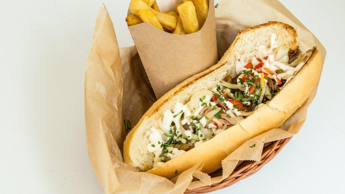 Ein frisch zubereiteter Sandwich mit Gemüse und Saucen in einem Korb. Dazu gibt es knusprige Pommes frites in einer Papiertüte. | © The Hungry Heart