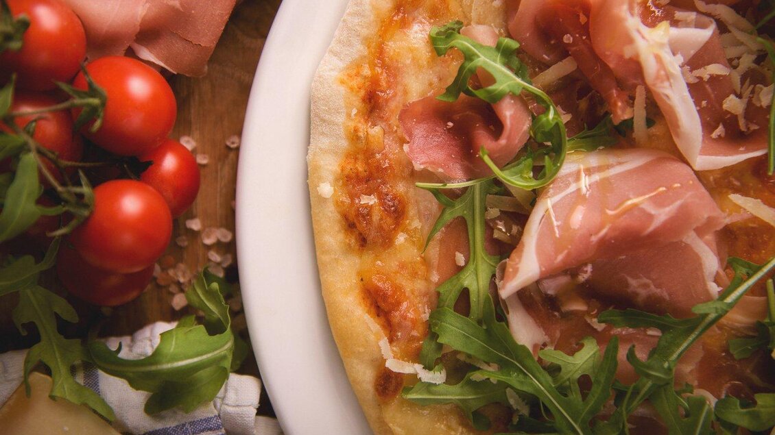 Eine leckere Pizza mit Schinken, Rucola und Käse. Dazu frische Kirschtomaten und Salz. | © The Kitchen