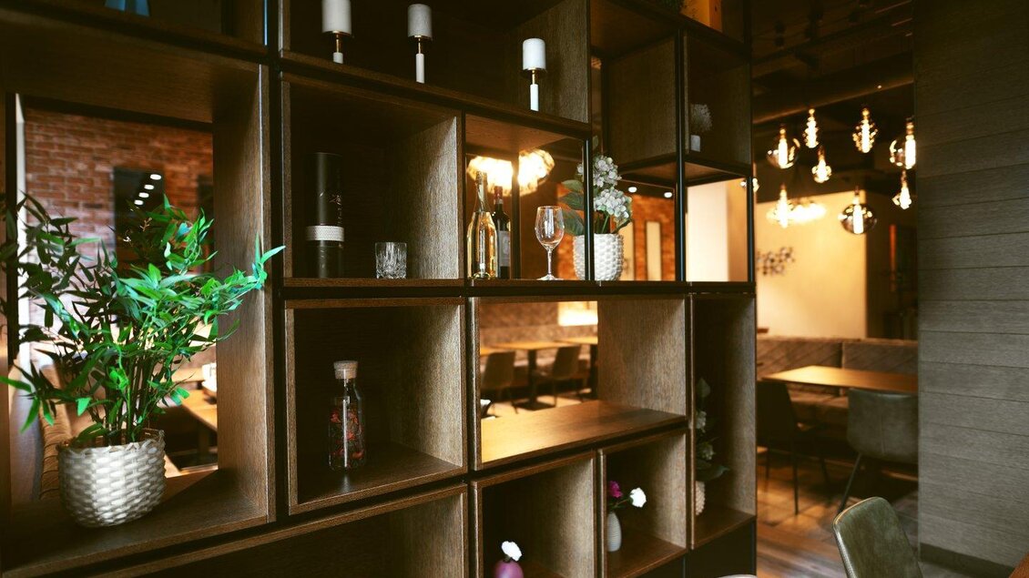 Ein modernes Restaurantinterieur mit einer dekorativen Holzregalwand. Pflanzen und stilvolle Beleuchtung schaffen eine einladende Atmosphäre. | © The Kitchen