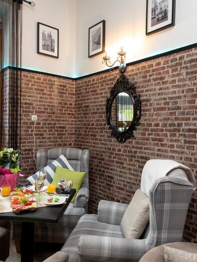 Gemütlicher Innenraum mit Ziegelsteinmauer, stilvollen Sesseln und einem roten Telefonhäuschen. Auf dem Tisch liegen frisches Obst und Snacks, umgeben von Pflanzen und Bildern an der Wand. | © TV Region Graz - Lunghammer