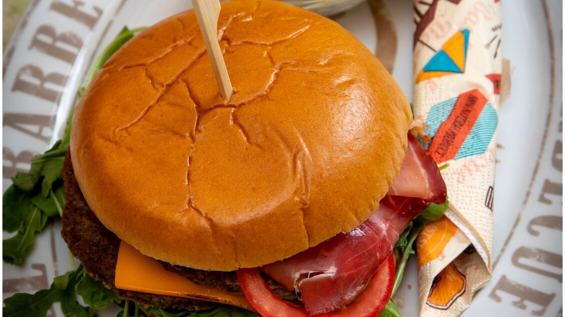 Ein saftiger Hamburger mit Käse, frischem Gemüse und einem knusprigen Brötchen. Serviert auf einem dekorativen Teller mit einer farbigen Serviette. | © TV Region Graz - Lunghammer