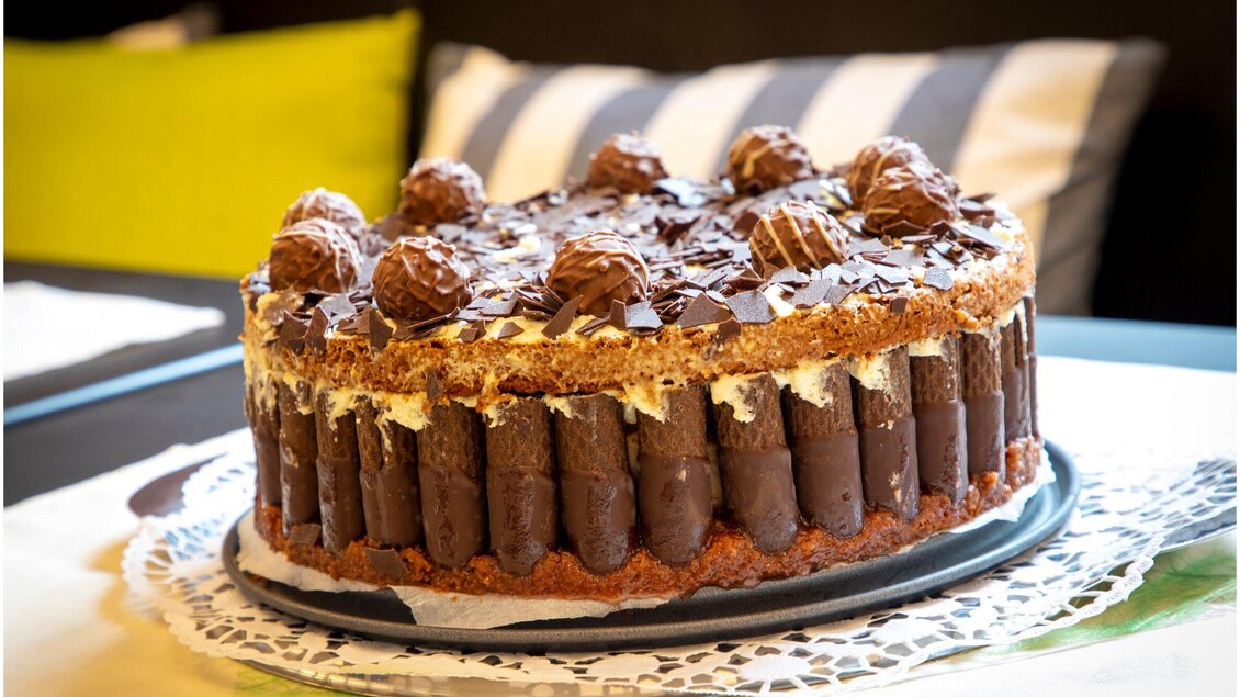 Eine köstliche Sahnetorte mit Schokoladengeschmack, dekoriert mit Schokoladenstückchen und Pralinen. Sie steht auf einem Serviettenring und ist von einem gemütlichen Ambiente umgeben. | © TV Region Graz - Lunghammer