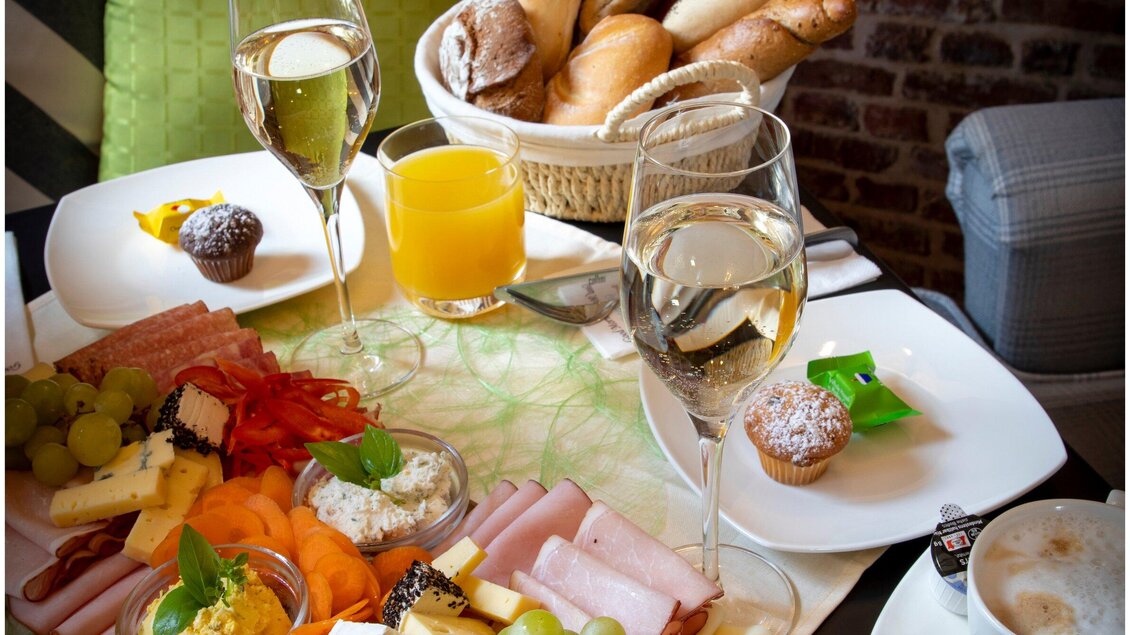 Ein reichhaltiges Frühstücksbuffet mit frischen Brötchen, Käsesorten, Wurst und Obst. Dazu Gläser mit Sekt und Orangensaft. | © TV Region Graz - Lunghammer