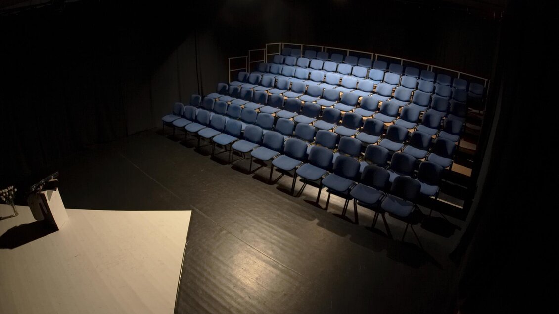 Ein leerer Zuschauerraum mit blauen Stühlen. Die Beleuchtung ist gedämpft und die Bühne ist sichtbar. | © THEO Studiobühne