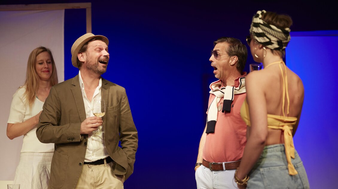 Eine Gruppe von vier Personen steht auf einer Bühne und interagiert miteinander. Die Atmosphäre ist lebhaft und freundlich. | © THEO Studiobühne