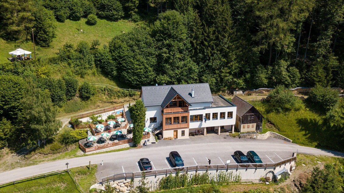 Ein schönes Gebäude inmitten von grünen Bäumen und Landschaft. Vor dem Haus sind Parkplätze und eine Außenterrasse mit Sitzmöglichkeiten zu sehen. | © TV Region Graz - Harry Schiffer