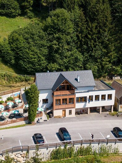 Ein schönes Gebäude inmitten von grünen Bäumen und Landschaft. Vor dem Haus sind Parkplätze und eine Außenterrasse mit Sitzmöglichkeiten zu sehen. | © TV Region Graz - Harry Schiffer