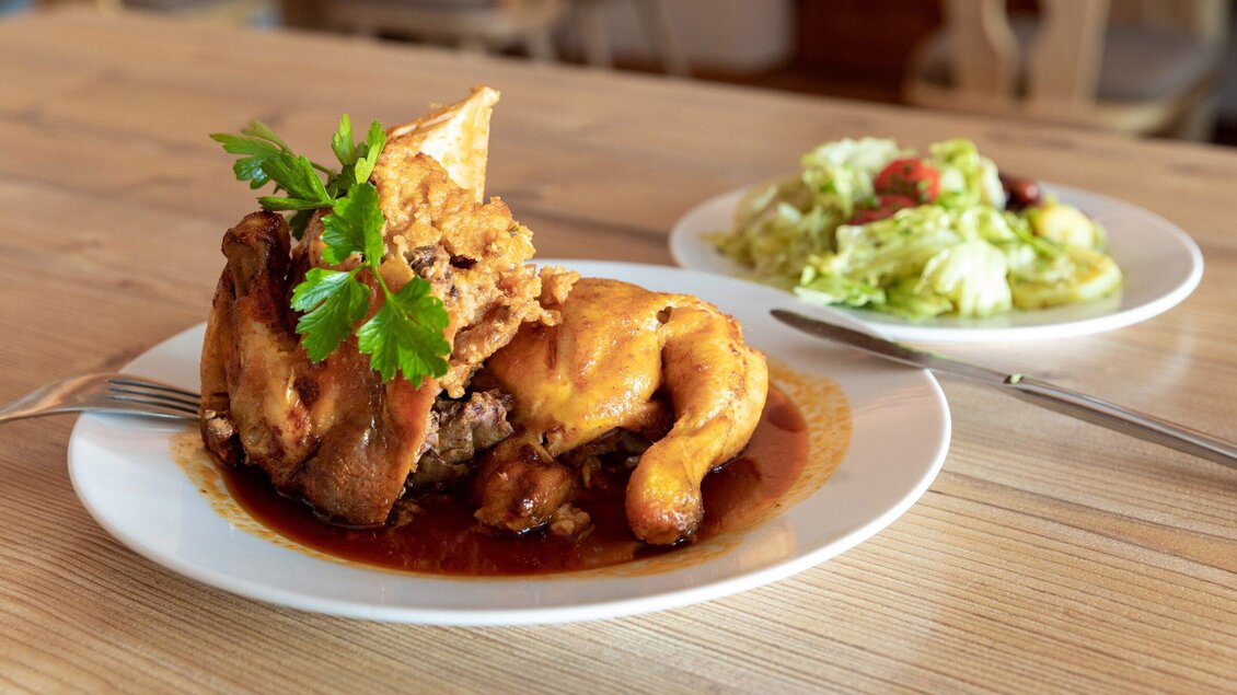 Ein knuspriges Hühnchen mit einer aromatischen Sauce, garniert mit frischer Petersilie. Neben dem Hühnchen liegt ein frischer Salat. | © TV Region Graz - Harry Schiffer