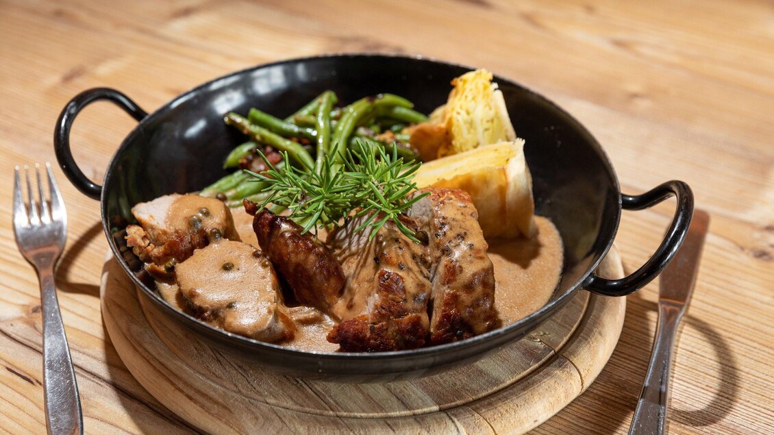 Ein leckeres Gericht in einer schwarzen Pfanne. Es besteht aus gebratenem Fleisch, grünen Bohnen und einem Stück Gemüsebeilage. | © TV Region Graz - Harry Schiffer