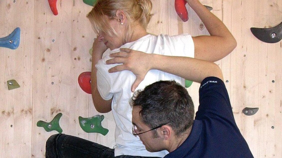 Eine Person klettert an einer Kletterwand, während eine andere Person Unterstützung bietet. Die Wände sind mit verschiedenen farbigen Griffen ausgestattet. | © Therapiezentrum Prä-Fit