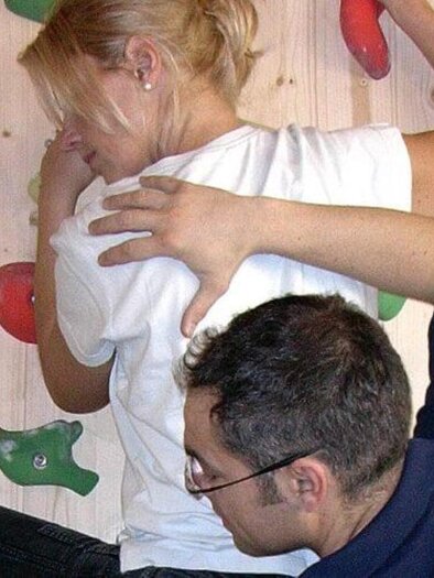 A person is climbing on a climbing wall while another person offers support. The walls are equipped with various colored holds. | © Therapiezentrum Prä-Fit