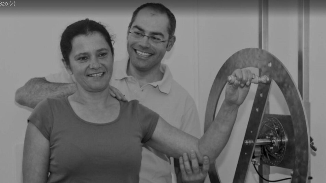 Eine Frau steht lächelnd neben einem Mann, während sie eine Maschine bedienen. Der Mann schaut freundlich und unterstützt sie dabei. | © Therapiezentrum Prä-Fit