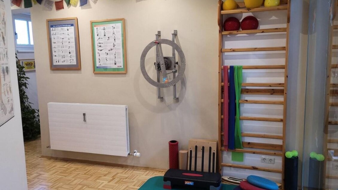 Ein helles Trainingszimmer mit Fitnessgeräten und Übungspostern an der Wand. An der Wand gibt es eine Kletterleiter und verschiedene farbige Bälle. | © Therapiezentrum Prä-Fit