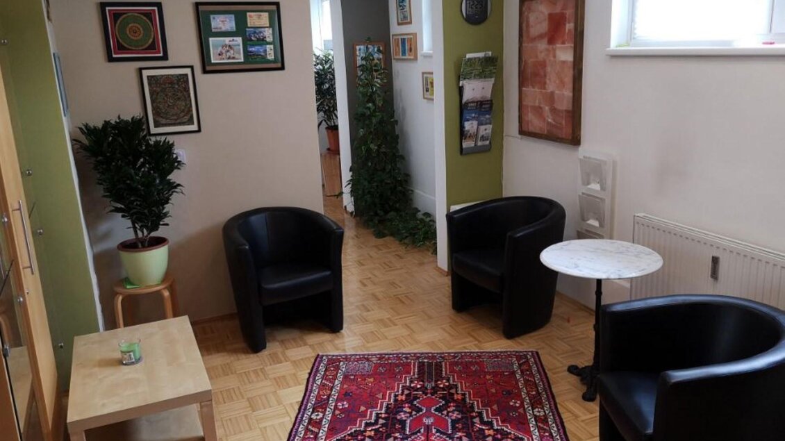 Ein gemütlicher Raum mit zwei schwarzen Sesseln und einem kleinen Tisch. An den Wänden hängen Bilder, und es gibt eine Pflanze in der Ecke. | © Therapiezentrum Prä-Fit