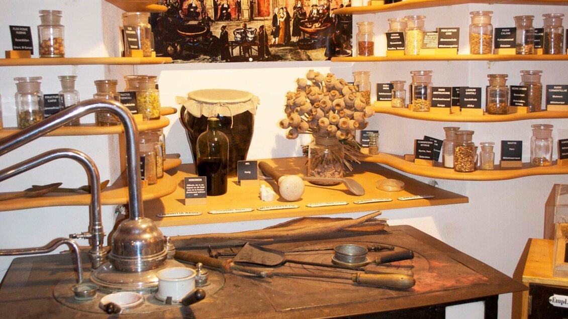 Eine historische Werkstatt mit verschiedenen Gläsern und Utensilien. Auf Regalen sind zahlreiche Kräuter und Gewürze ausgestellt. | © Theriak Museum