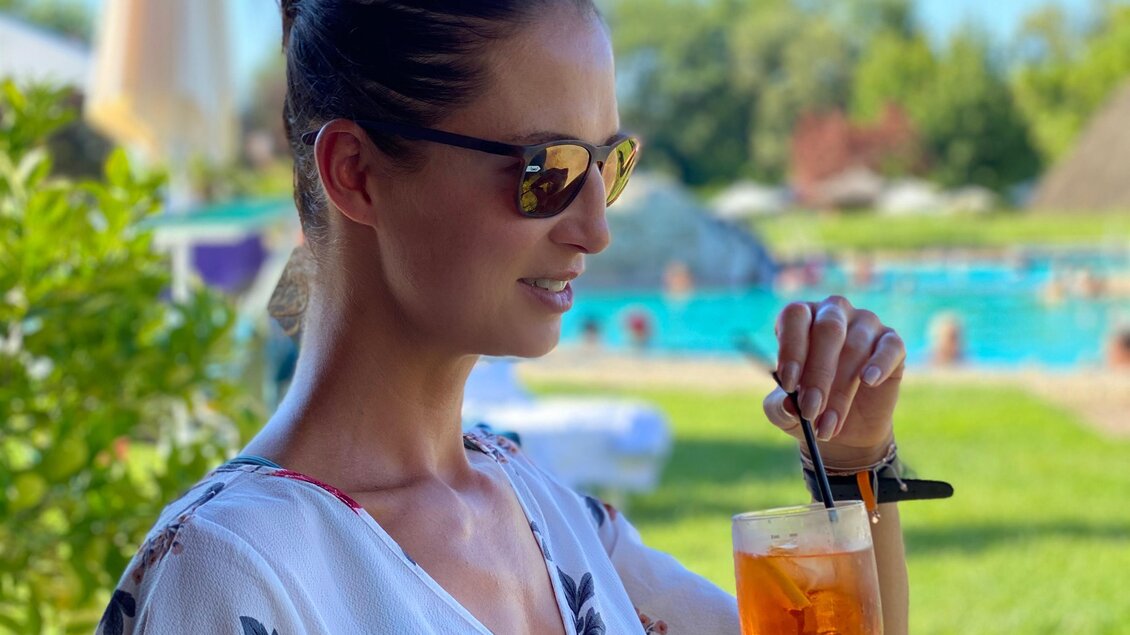 Eine Frau genießt ein Getränk am Pool. Sie trägt eine Sonnenbrille und ein helles, blumiges Oberteil. | © silviaschreibt.de