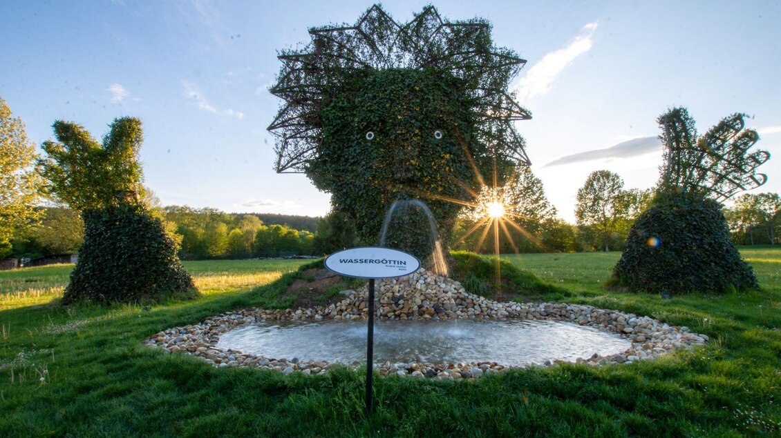 Eine kunstvolle Gartenlandschaft mit Skulpturen aus Pflanzen, die Tiere darstellen. In der Mitte befindet sich ein kleiner Teich mit einer sprudelnden Quelle. | © Kurkommission Bad Blumau